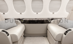 Close up of drinkrail with dark wood accent between two cream leather chairs in refurbished Falcon 7X