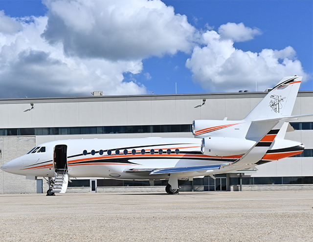 Photo of Falcon 900 with open door sitting in front of a Duncan Aviation hangar painted in white with orange and navy stripe