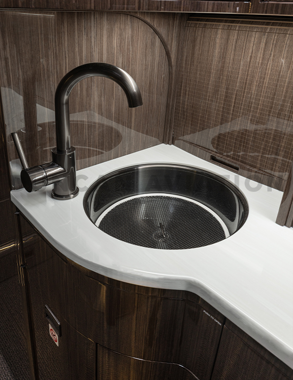 Refurbished sink in galley of Falcon 900 with white counters, dark wood and burnished metal finish