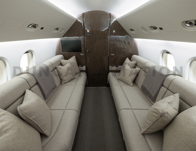 Two divans facing each other in cool beige leather with dark carpet and dark wood on Falcon 900 refurbished by Duncan Aviation
