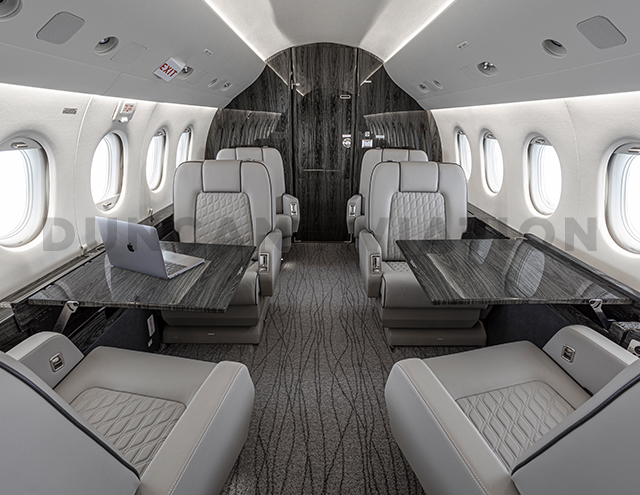 Gray club seats with conference tables inside Falcon 2000